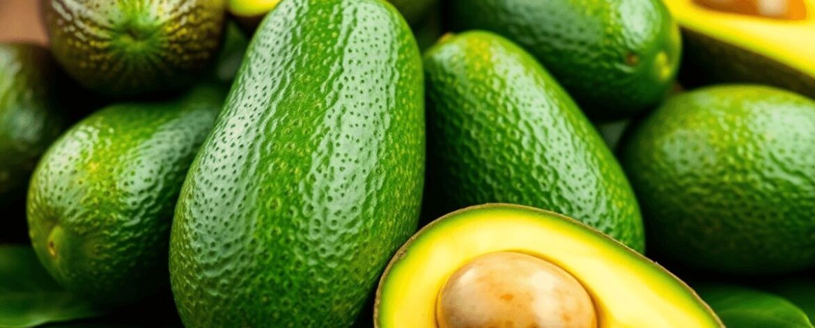 Close-up of fresh Hass and Fuerte avocados with green leaves on a rustic wooden table, showcasing high-quality produce.